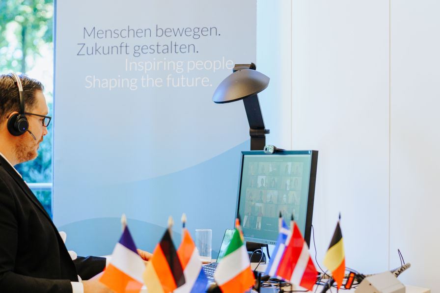 Moderator vor dem Bildschirm, im Vordergrund europäische Flaggen